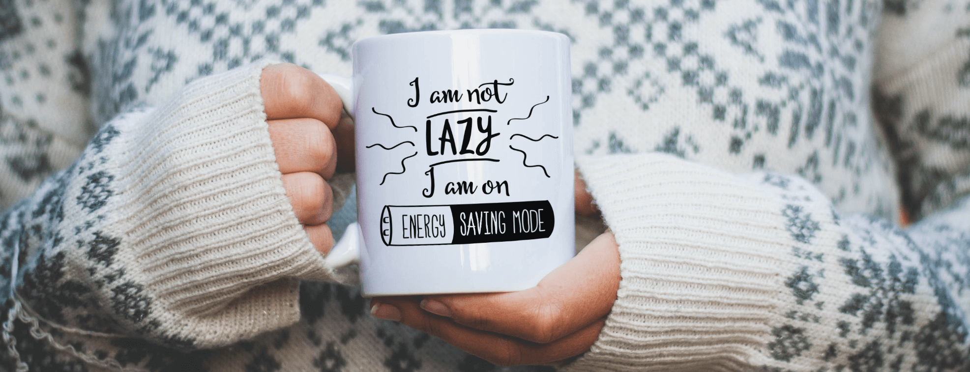 A girl in a cozy sweater holding a mug with 'I am not lazy I am on energy saving mode' written on it